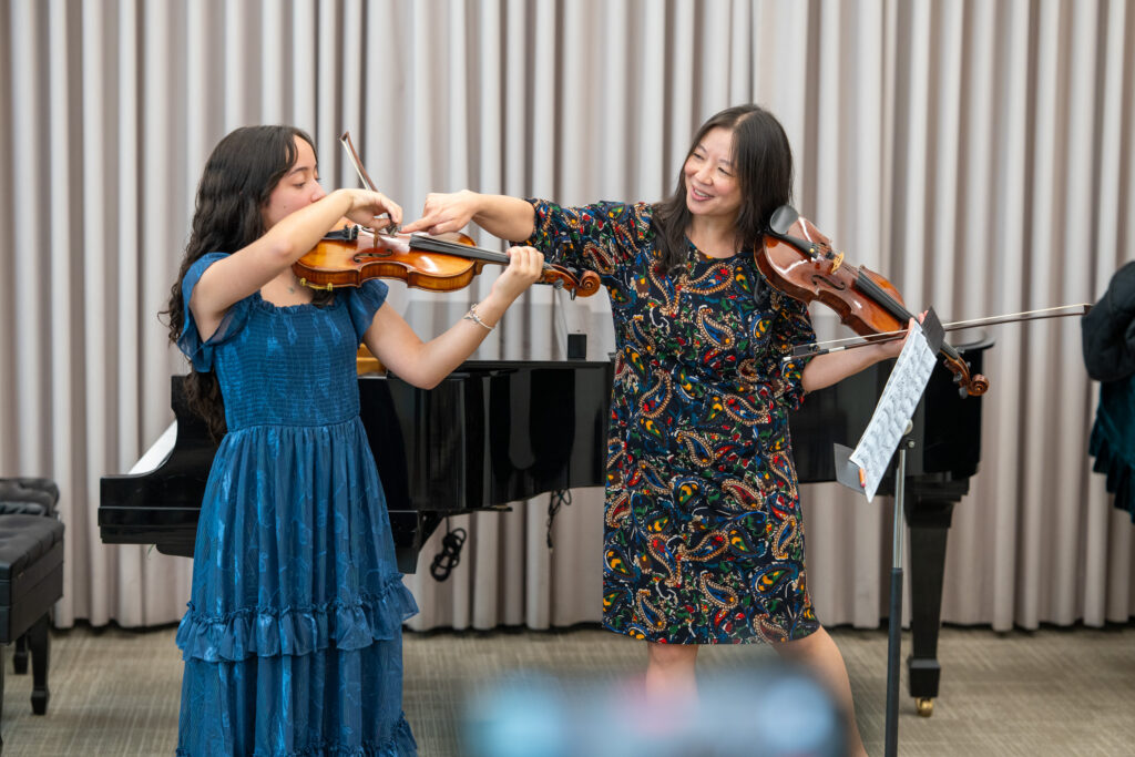 Maureen Yuen adjusts a student violinist's hand position as both play side by side
