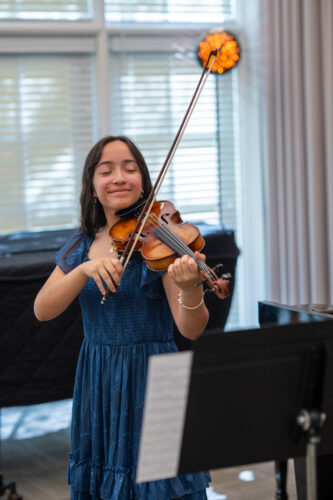 A student violinist in a blue dress plays with eyes closed