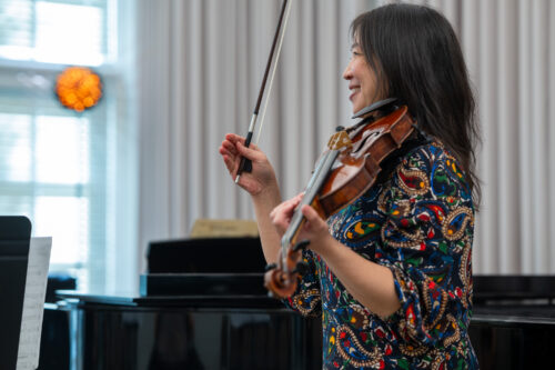 Maureen Yuen smiles while demonstrating with her violin and bow