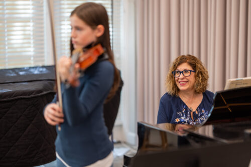 A collaborative pianist smiles at the piano as a young violinist performs