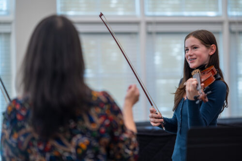 A smiling student violinist responds to coaching from Maureen Yuen