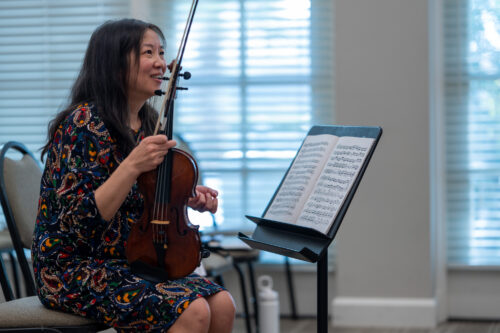 Maureen Yuen, seated with her violin, smiles while giving feedback